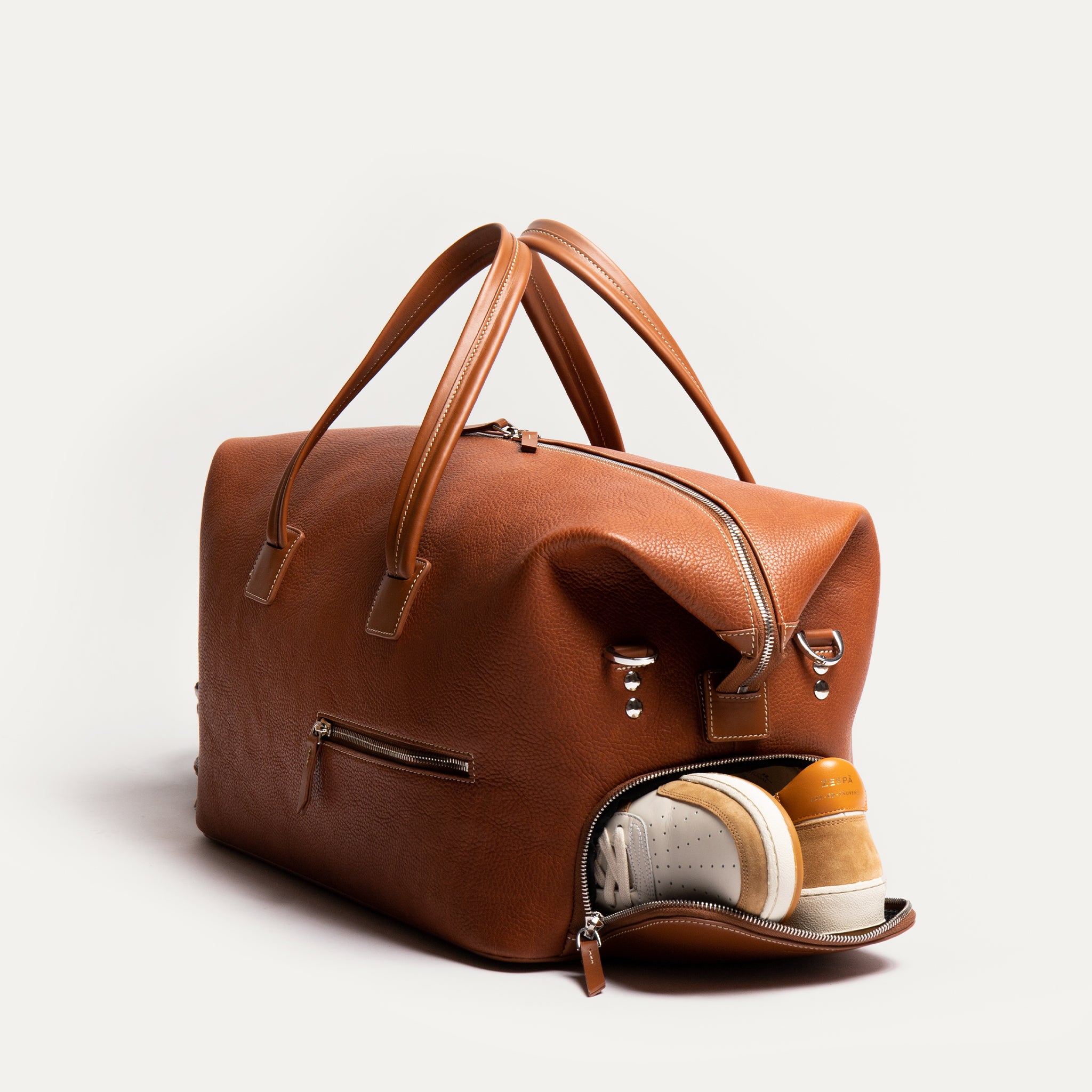 Partez en voyage avec ce sac en cuir cognac doté de poches multiples, dont un compartiment pour chaussures. Idéal pour organiser vos affaires avec style, ce sac est parfait pour les escapades de week-end ou les voyages d'affaires.