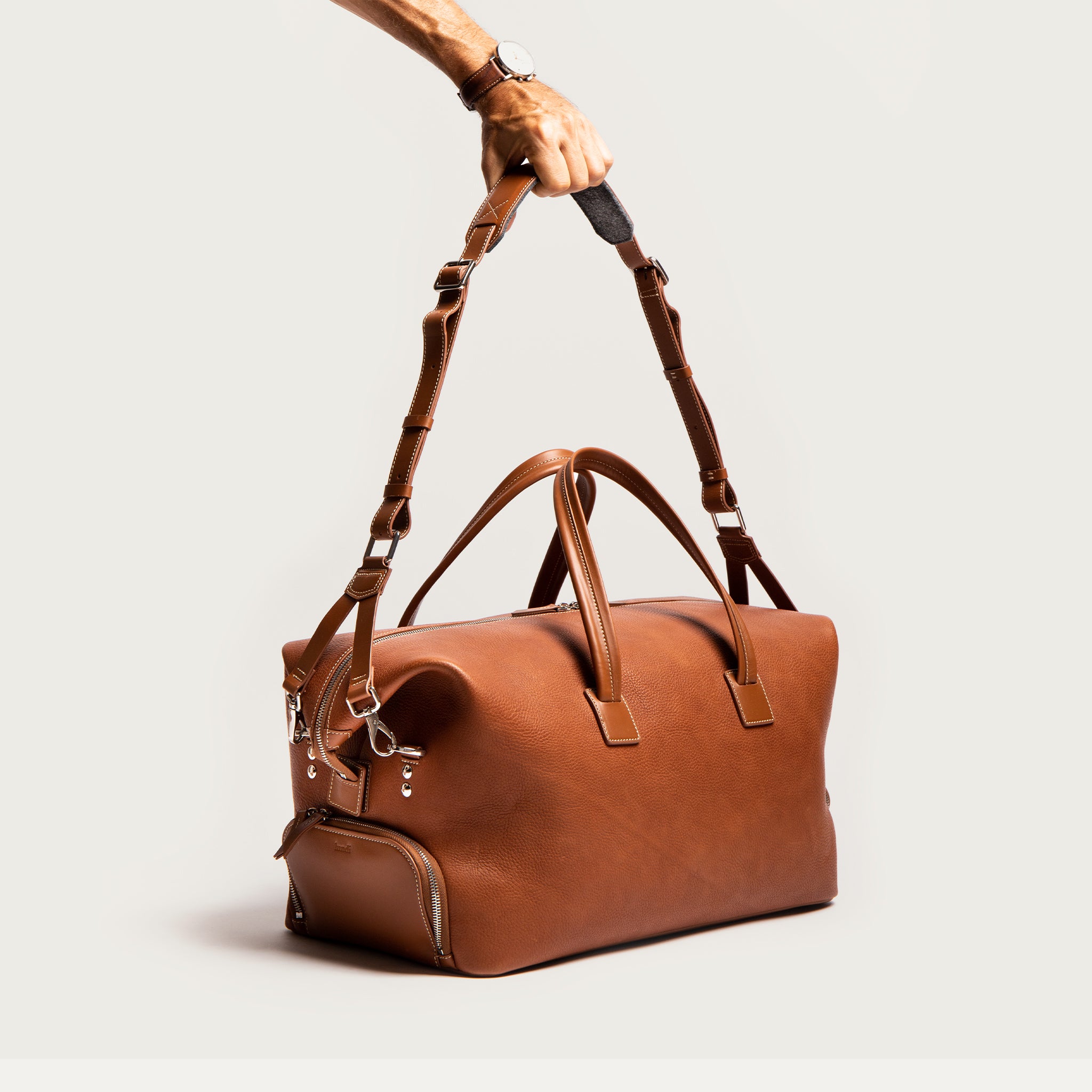 ce sac de voyage en cuir camel comporte des anses pour le porter à la main et une sangle en cuir réglable pour un porté épaule. lors du transport ce sac offre un maximum de confort lors de vos voyages. 